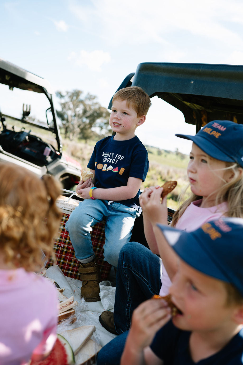 Kids having smoko on the back of a farm ute, one wearing the WHAT'S FOR SMOKO? kids t-shirt
