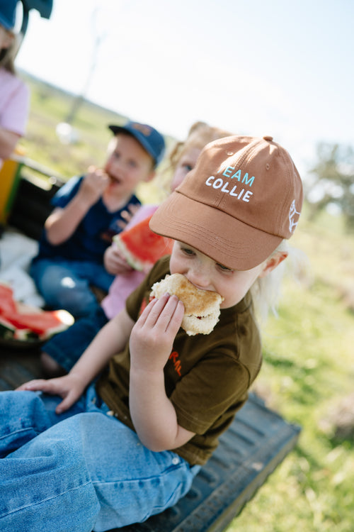 Child eating smoko outdoors wearing the coffee TEAM COLLIE kids cap